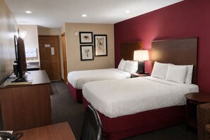 Une chambre d’hôtel avec deux lits, un bureau avec un ordinateur, une chaise, une lampe et des tableaux encadrés au mur.