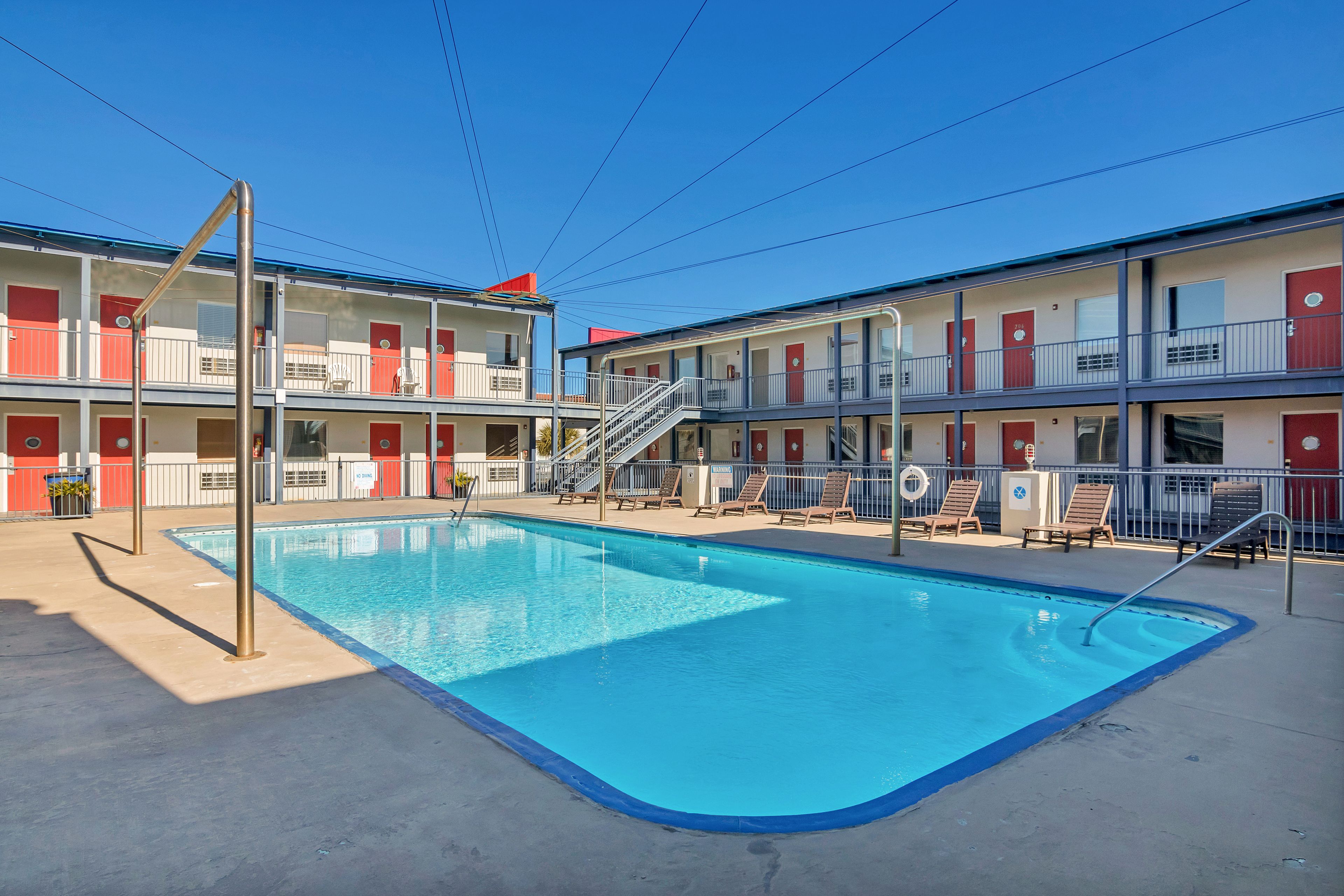 A motel with a swimming pool, multiple balconies, and a clear blue sky.