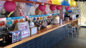 A bar area with a colorful mural, various drink dispensers, and a counter with chairs. - Sea And Breeze Hotel And Condo (Tybee Island)