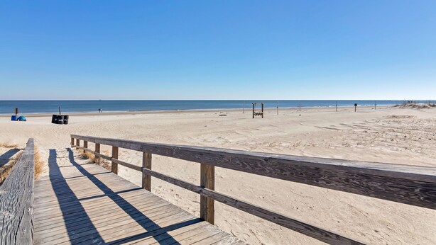 A wooden boardwalk leading to a sandy beach with a clear blue sky. - Sea And Breeze Hotel And Condo (Tybee Island)