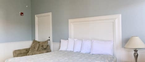 A bedroom with a bed, a nightstand, a lamp, a ceiling fan, and a door.