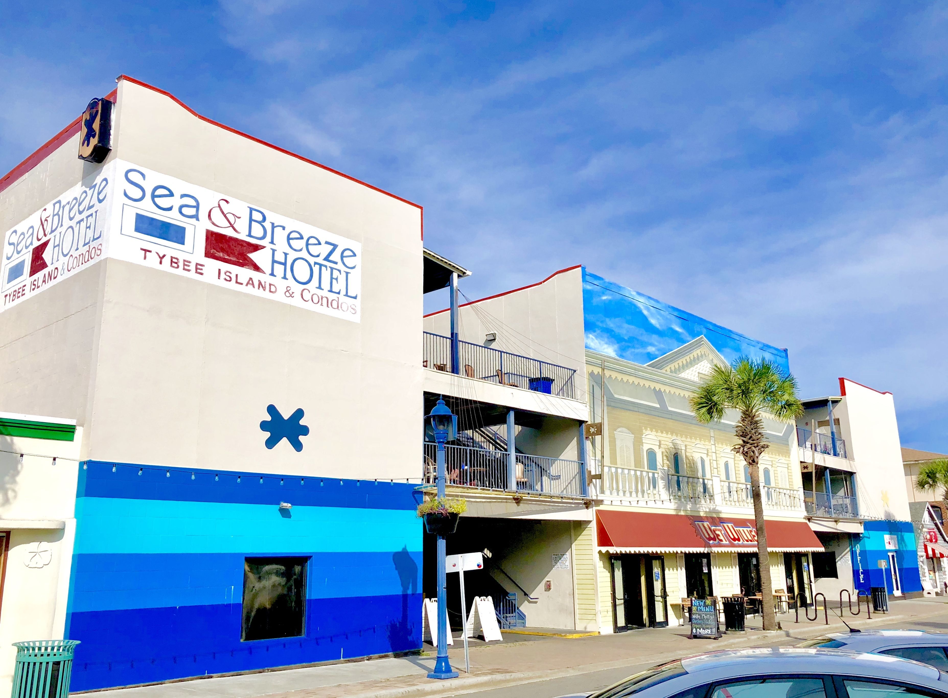 A hotel named Sea & Breeze Hotel with a blue and white facade, balconies, and a sign for Tybee Island & Condos.