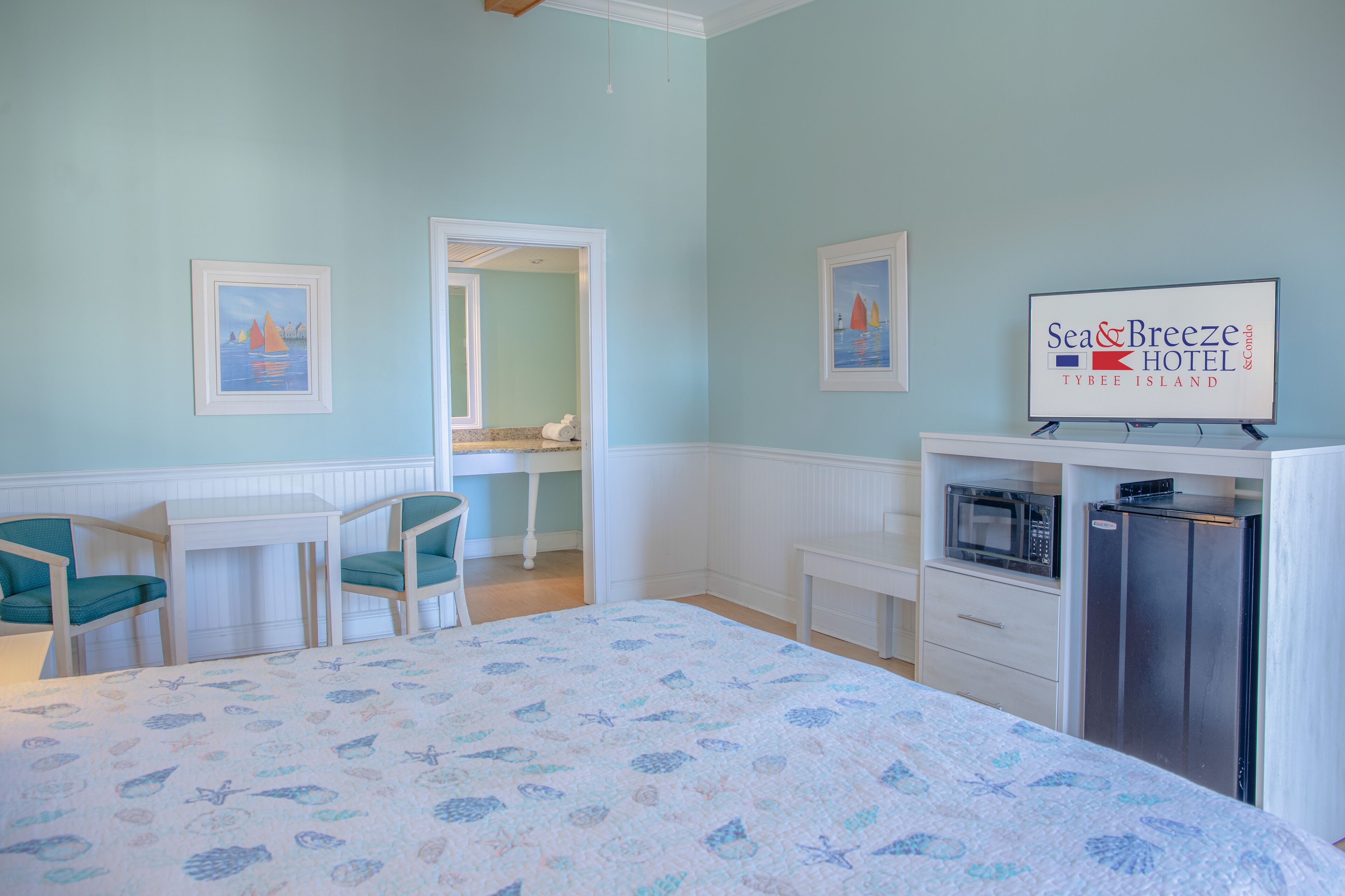 A bedroom with a bed, two chairs, a desk, a mirror, a microwave, and a refrigerator.