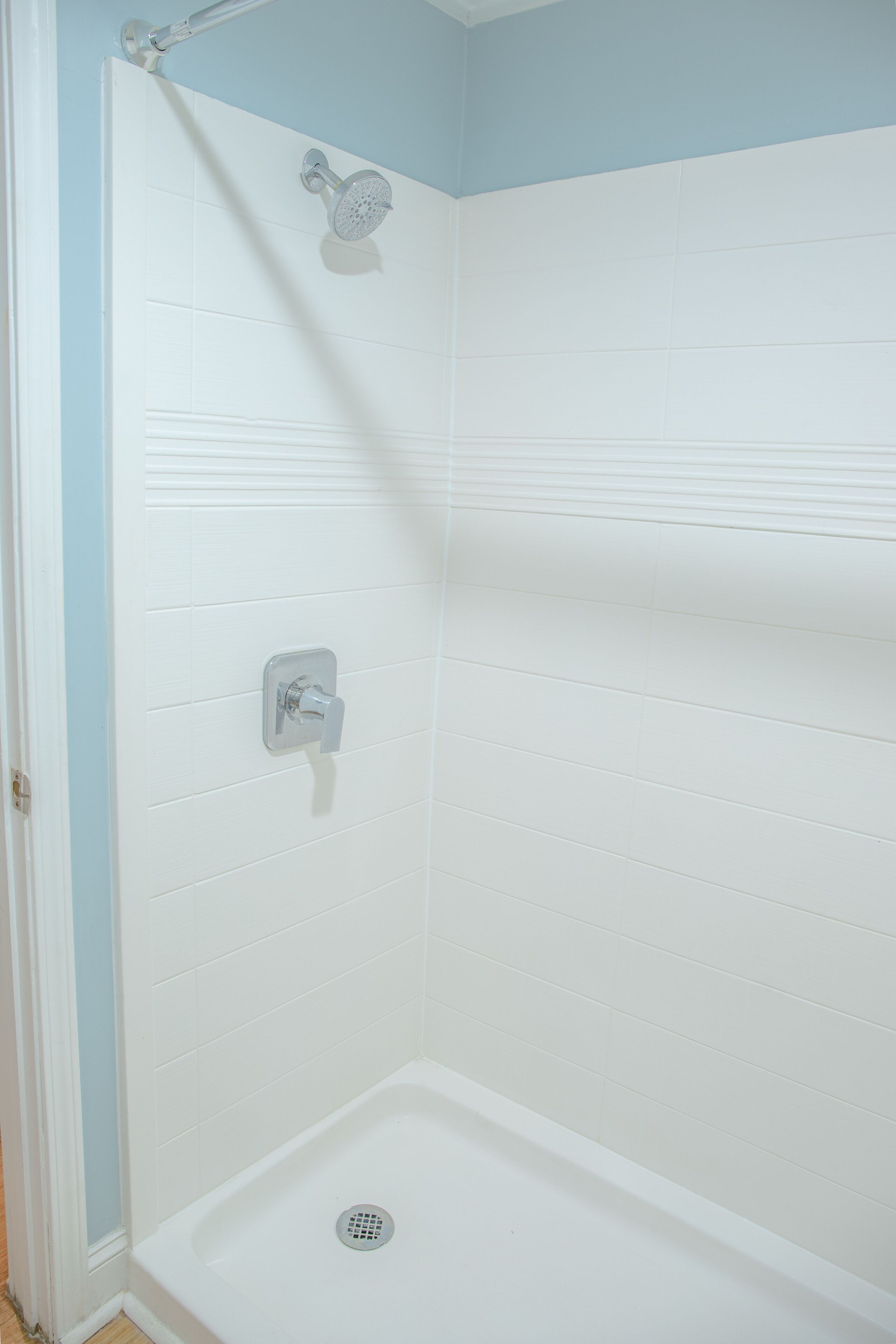 A walk-in shower with white tiles, a showerhead, and a drain.