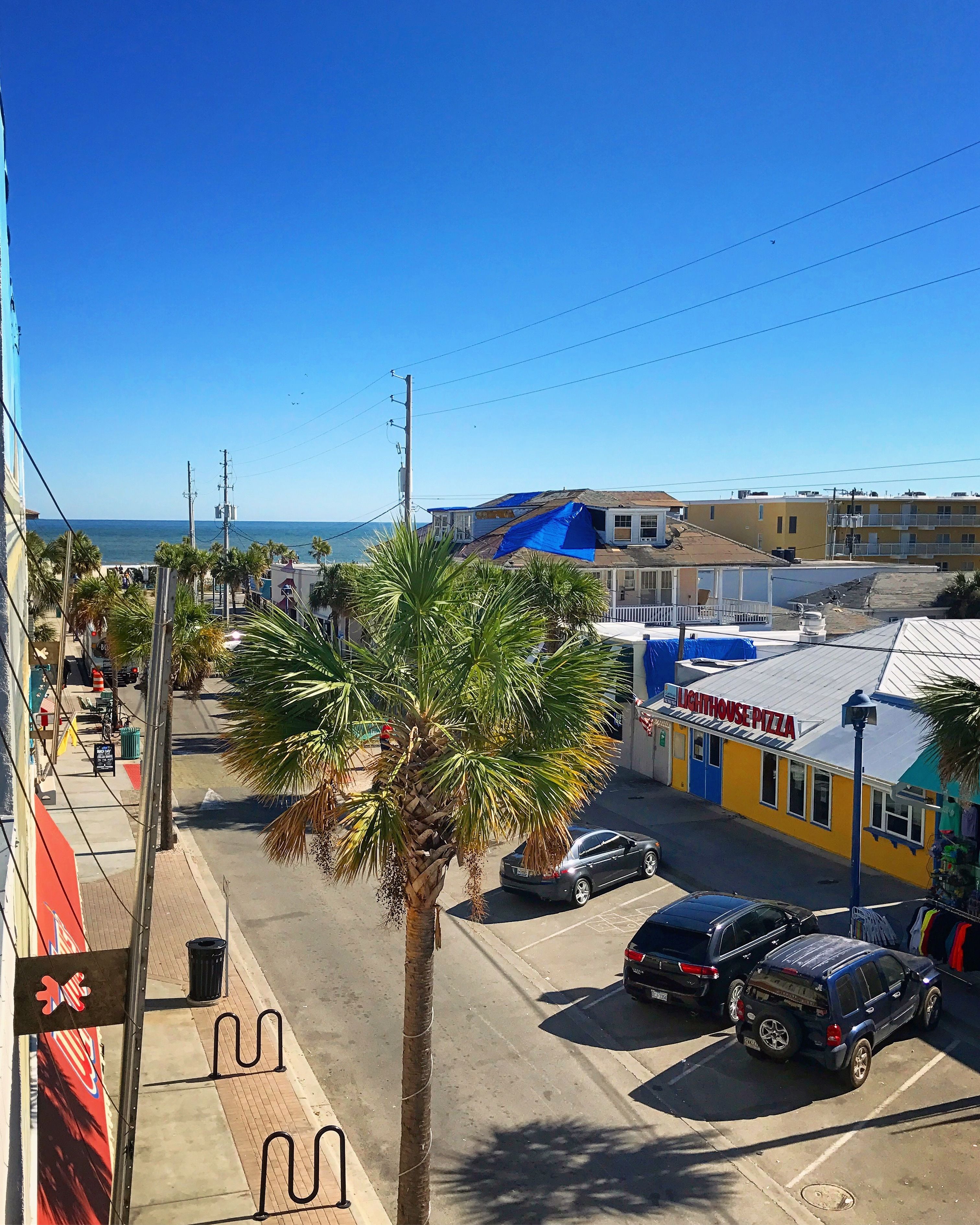 A street view with a building named "Lighthouse Pizza" and a palm tree in the foreground.