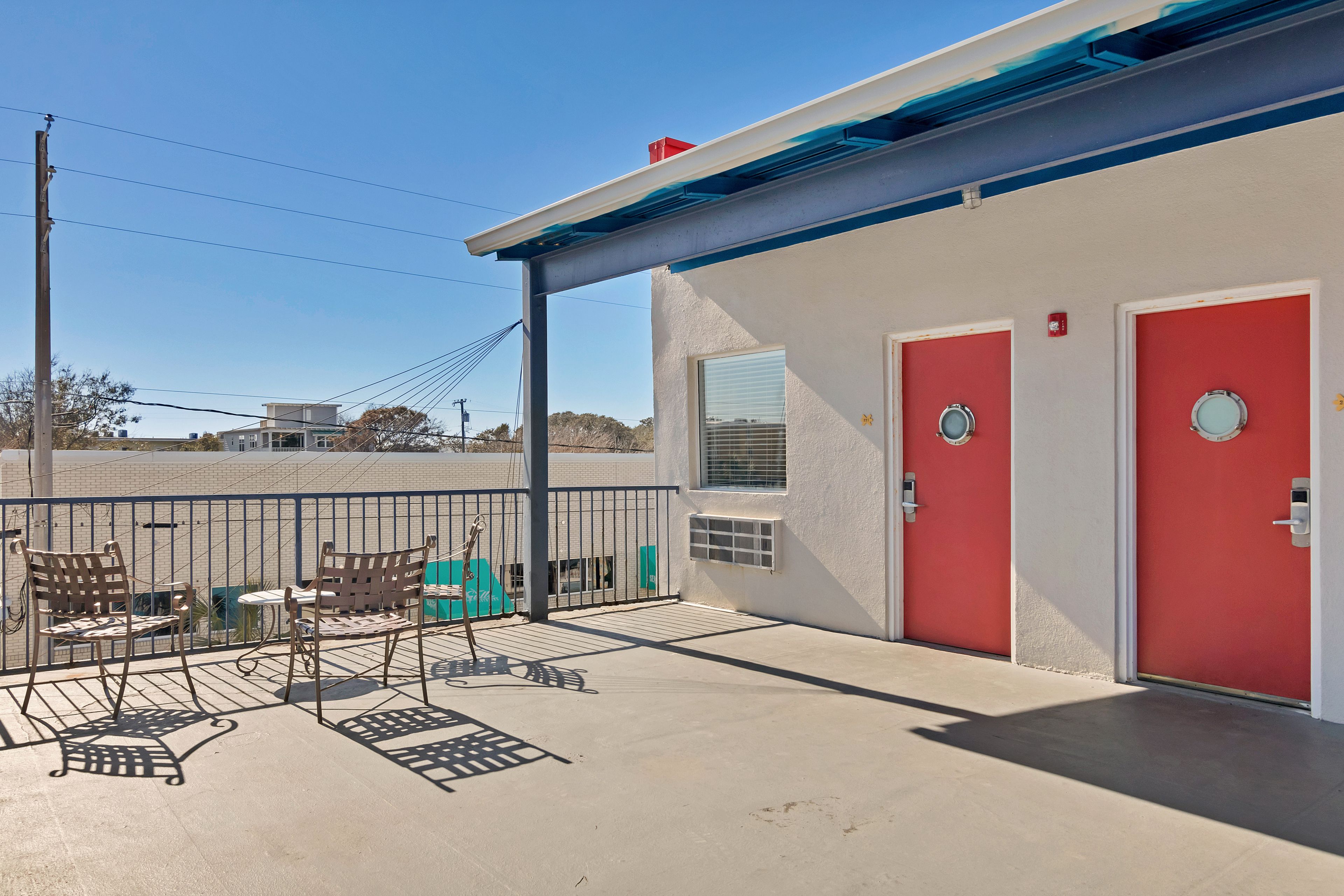 A building with two red doors, a covered outdoor area with metal chairs, and a concrete floor.
