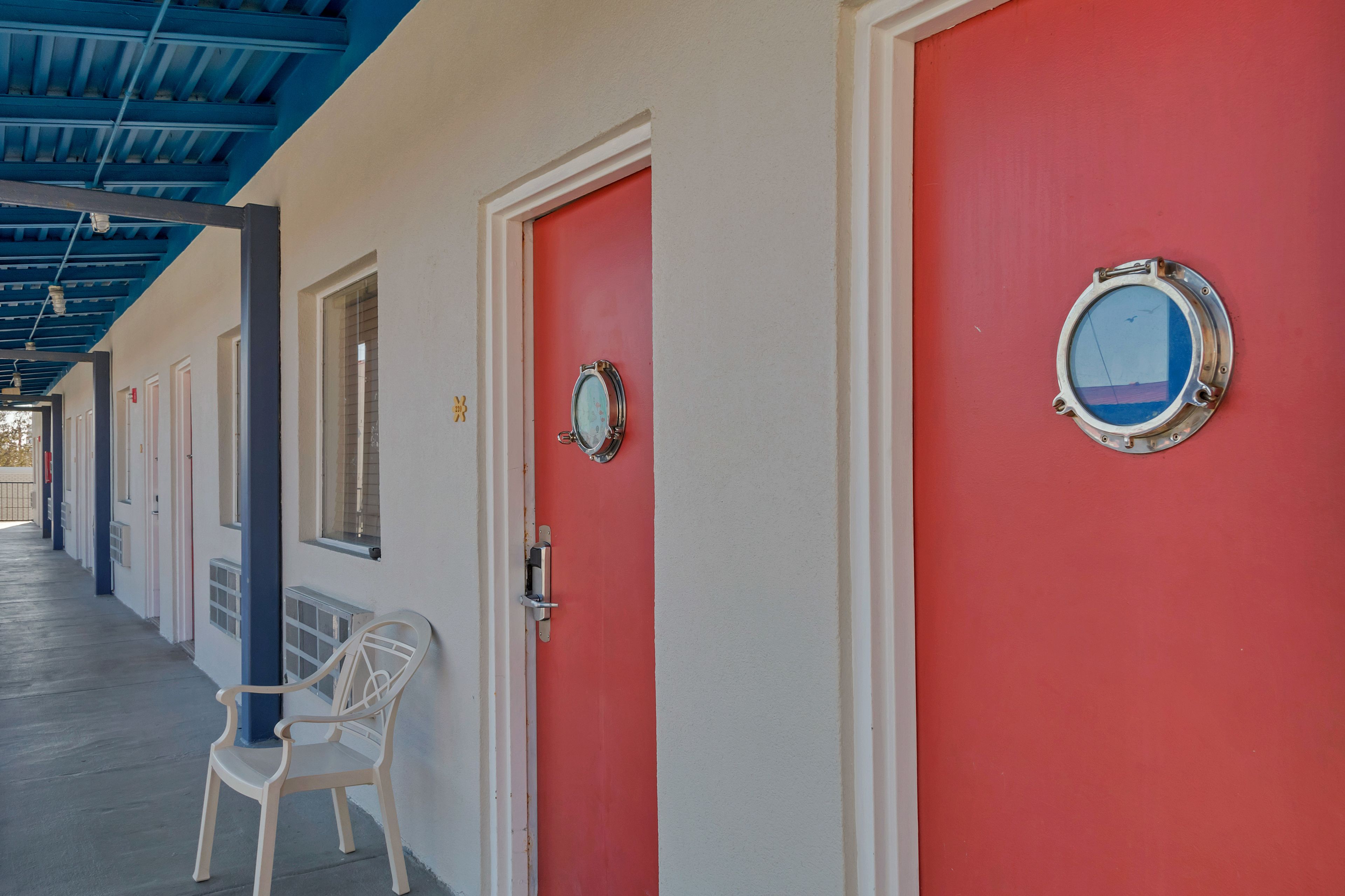 Um corredor com portas vermelhas, uma cadeira branca e teto azul.