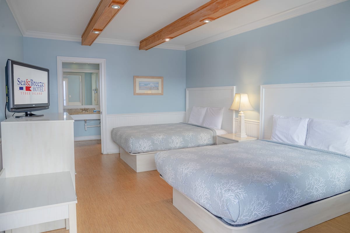 A hotel room with two beds, a TV, a desk, and a bathroom visible through an open door.