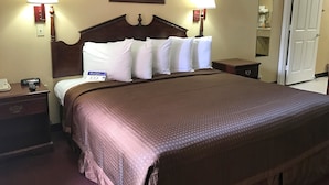 Ein Hotelzimmer mit einem großen Bett, zwei Nachttischlampen, einem Nachttisch mit Telefon und einem gerahmten Bild an der Wand.