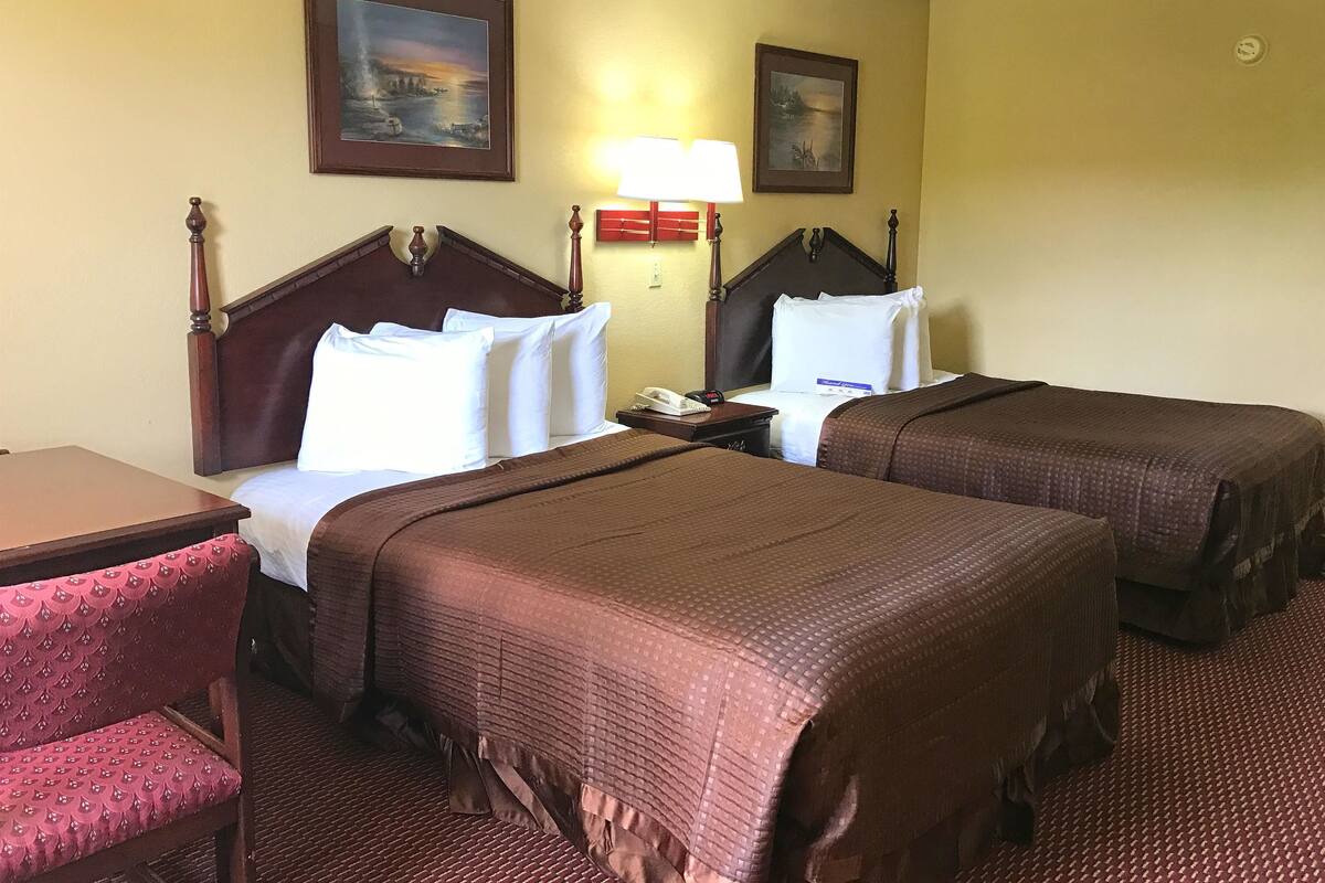 Ein Hotelzimmer mit zwei Betten, einem Schreibtisch, einem Stuhl und zwei Bildern an der Wand.