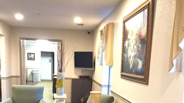 Eine Hotellobby mit Teppichboden, einem an der Wand montierten Fernseher und einem gerahmten Gemälde über einer Sitzecke.