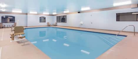 A large indoor swimming pool with clear blue water, a diving board, and a few lounge chairs.