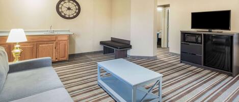 Habitación de hotel con sofá, una mesita, microondas, televisor, reloj y kitchenette.