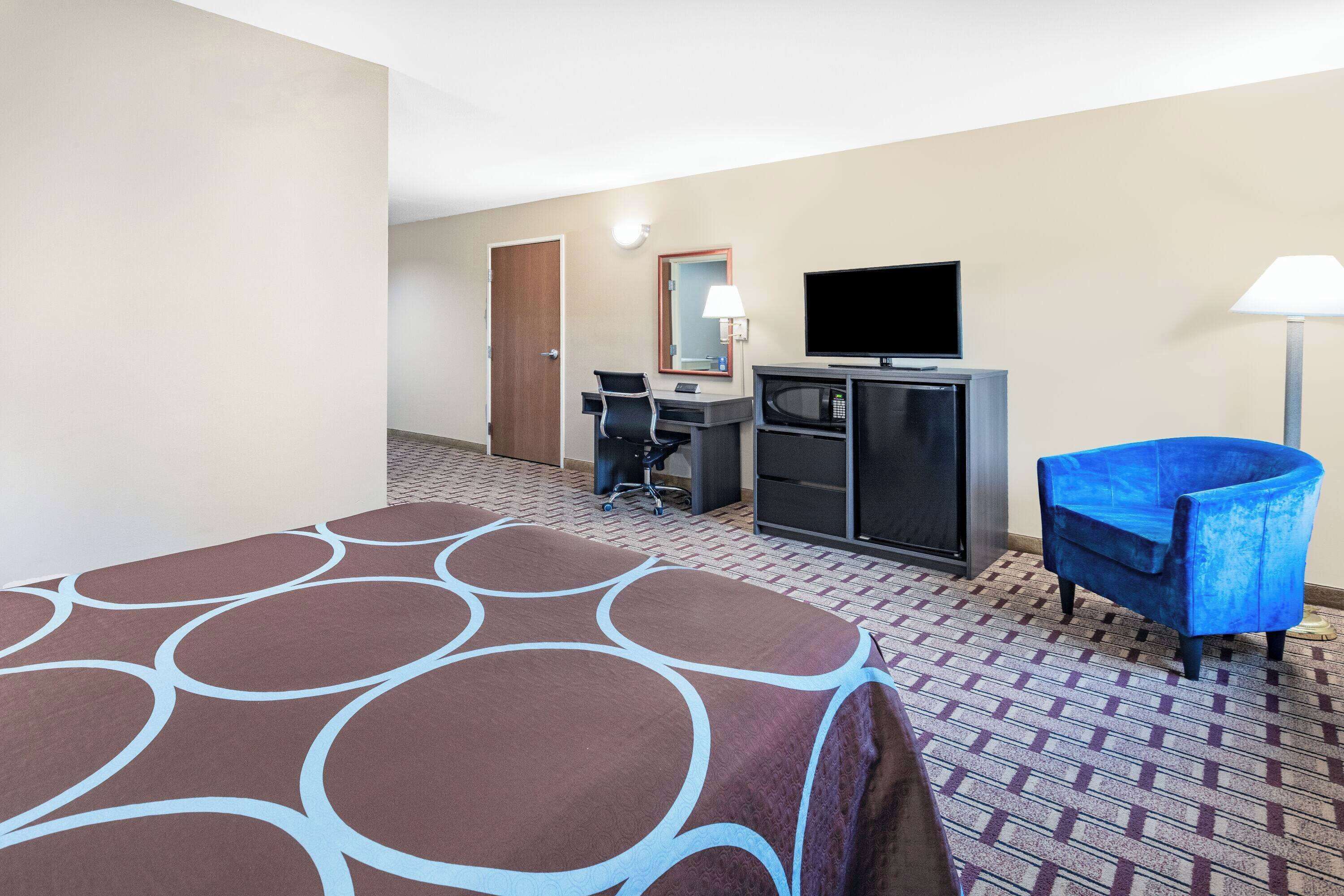 A hotel room with a bed, a desk, a television, a chair, and a lamp.