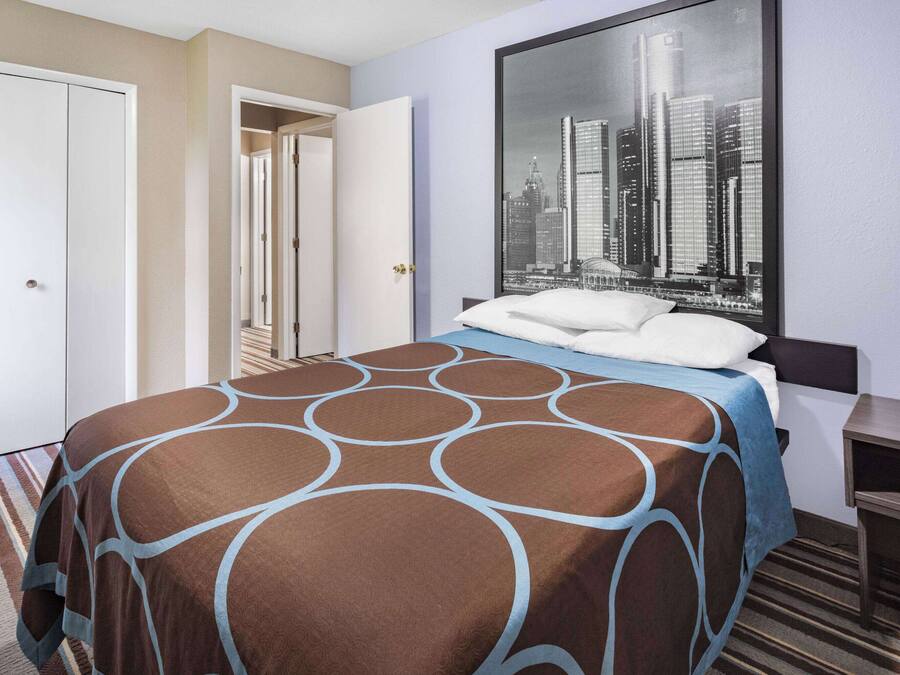 A hotel room with a bed, a cityscape view, a wardrobe, and a desk.