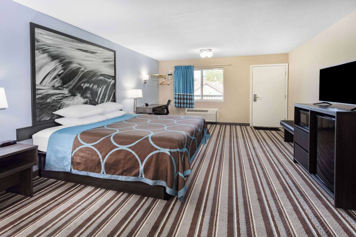 Habitación de hotel con una cama grande, un escritorio, un televisor y una ventana con cortinas.