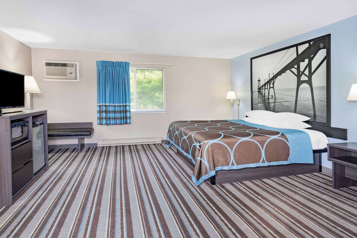 Una habitación de hotel con cama, televisión, escritorio y ventana con cortinas.