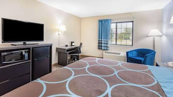 A hotel room with a flat-screen TV, a microwave, a refrigerator, a desk with a chair, a large bed with a patterned bedspread, a window with curtains, and a standing lamp.