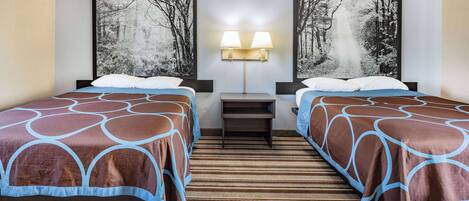 A hotel room with two beds, a nightstand, a lamp, and two large forest-themed wall art pieces.