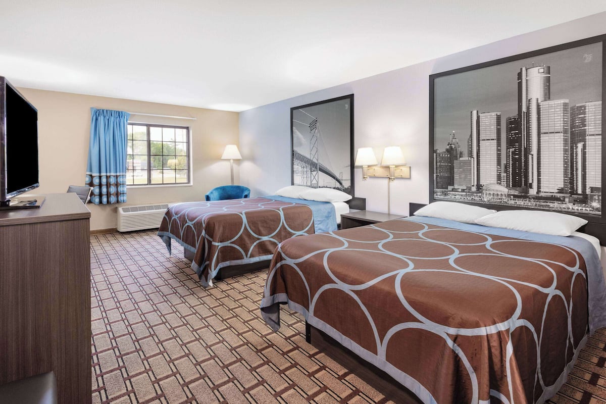 Habitación de hotel con dos camas, un escritorio, un televisor y vistas a la ciudad.