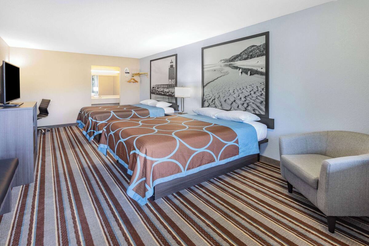 Habitación de hotel con cama, una silla, un escritorio con televisor y dos cuadros en la pared.
