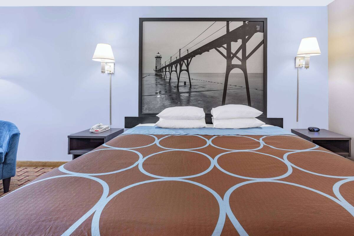 Una habitación de hotel con una cama grande, dos mesitas de noche, una lámpara de pared y una silla azul.