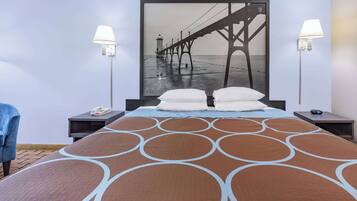 A hotel room with a large bed, two bedside tables, a nightstand, a blue chair, and a wall-mounted lamp.