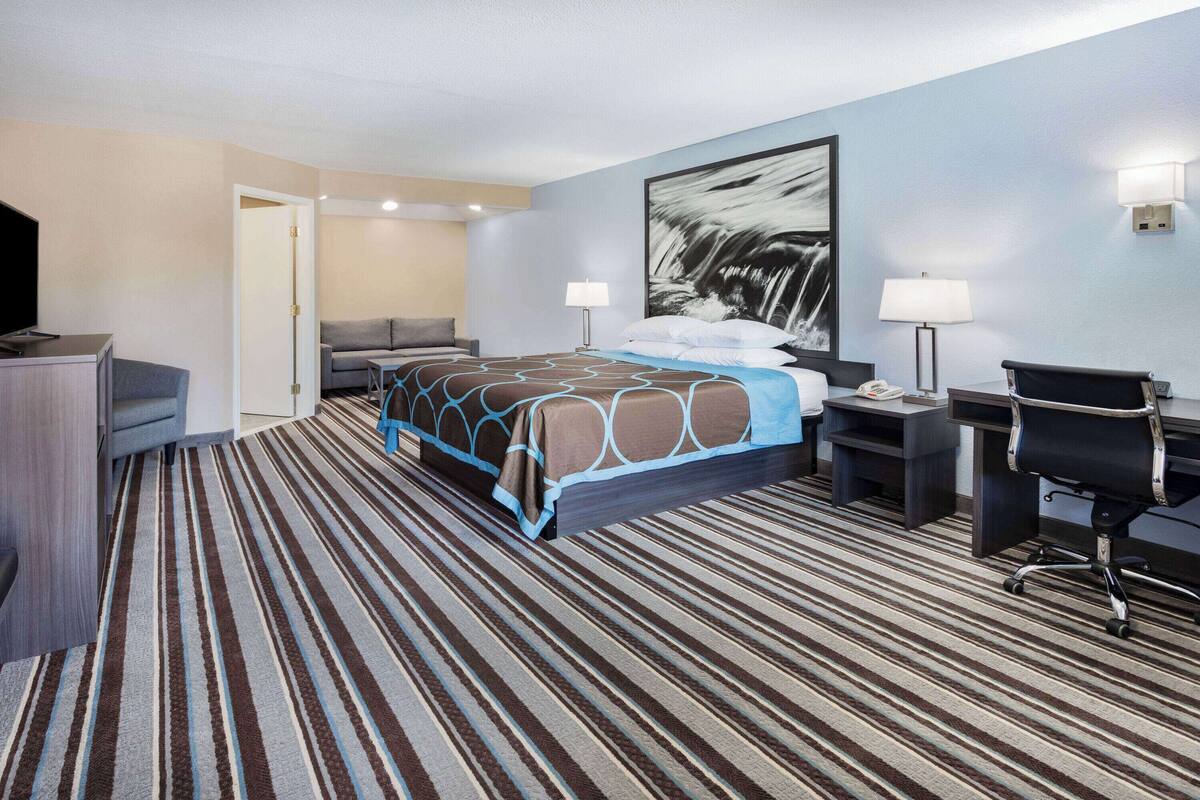 Una habitación de hotel con cama, escritorio, silla y un cuadro abstracto grande en la pared.