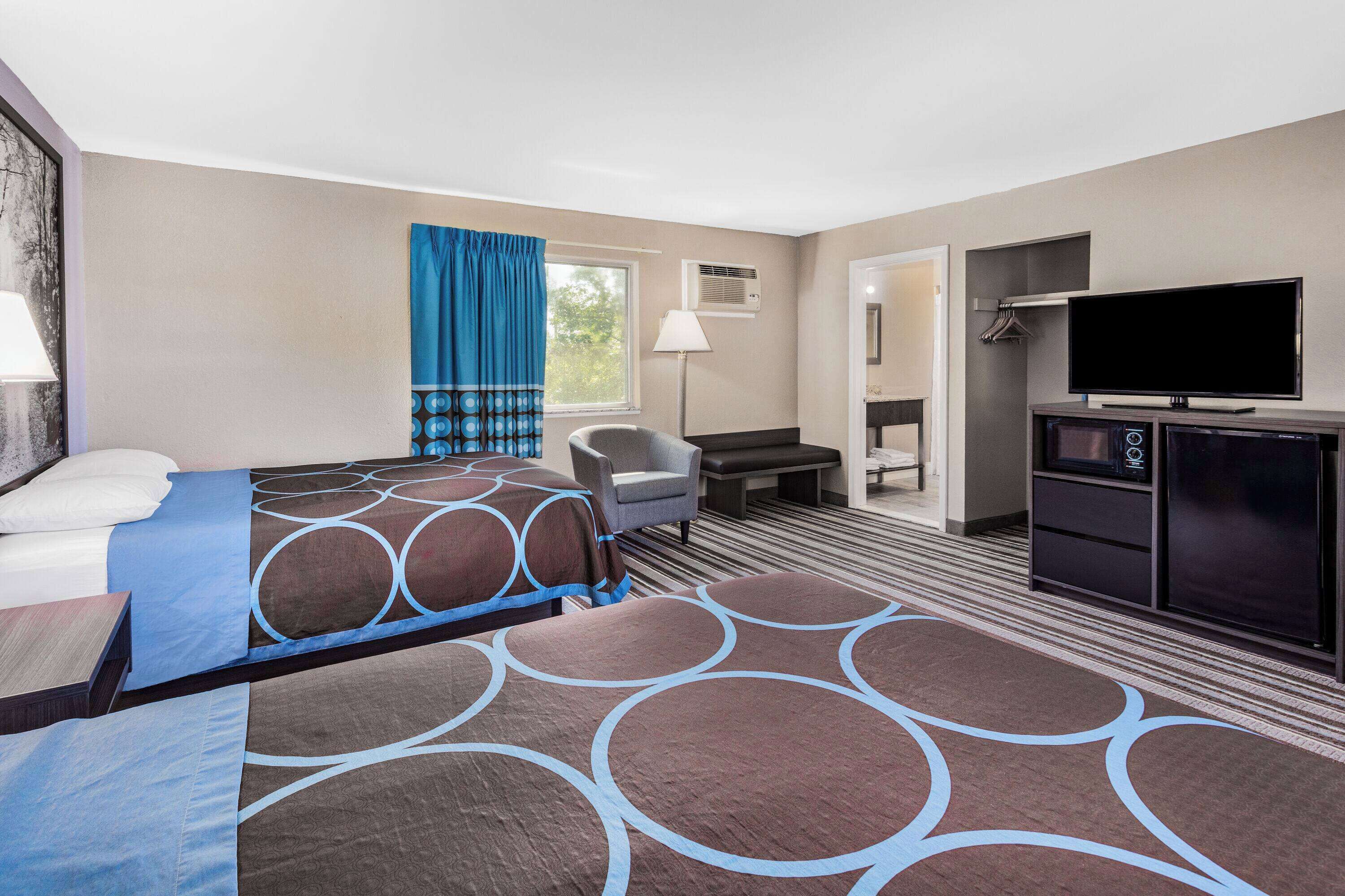 A hotel room with two beds, a desk, a chair, a TV, and a wardrobe.