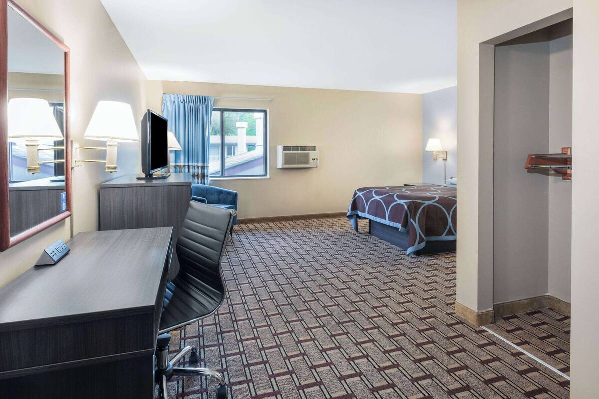 Una habitación de hotel con escritorio, cama, televisión y ventana con cortinas.