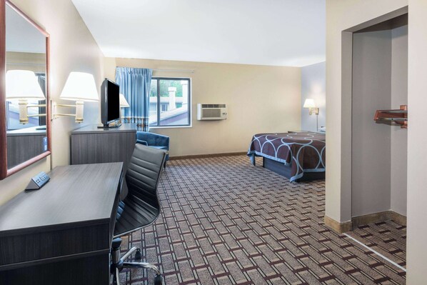 Una habitación de hotel con escritorio, cama, televisión y ventana con cortinas.