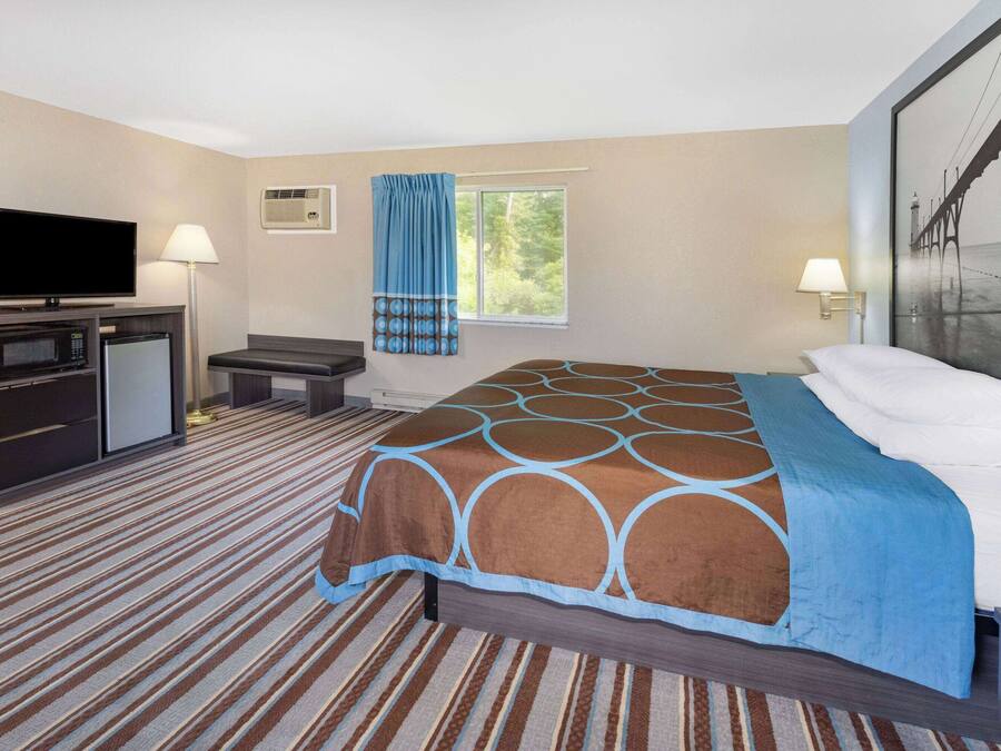 A hotel room with a bed, a TV, a desk, and a window.