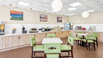 A modern cafe with a clean, minimalist design, featuring a white ceiling, wooden cabinets, and green chairs.