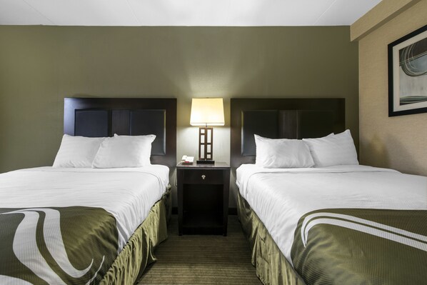 Habitación de hotel con dos camas, una mesita de noche con lámpara y un cuadro en la pared.