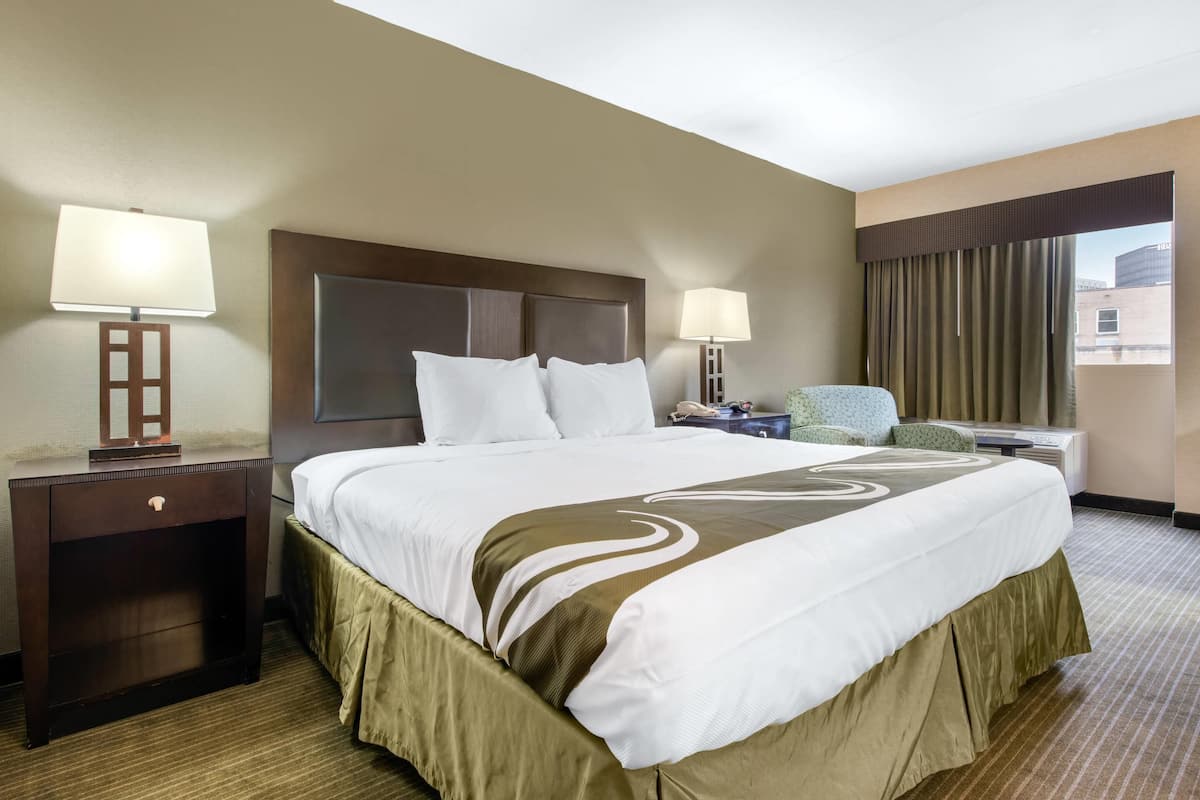 A hotel room with a large bed, two bedside tables with lamps, a chair, and a view of the outside.