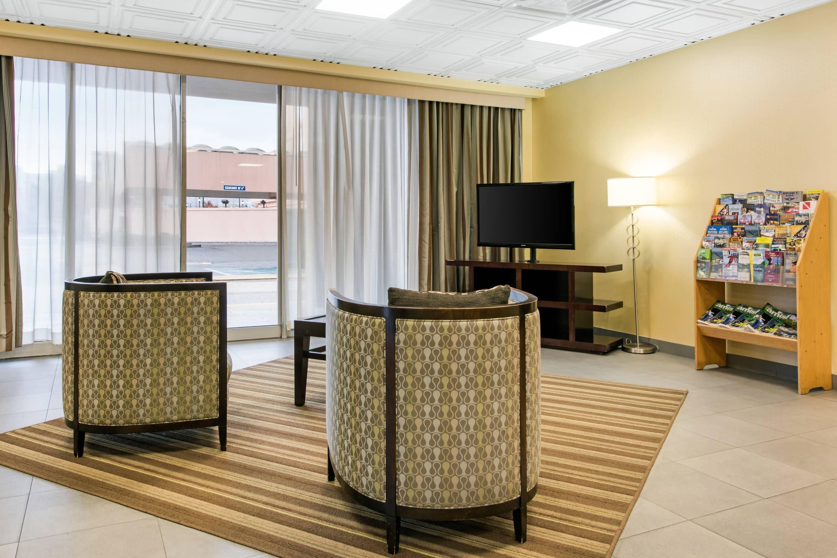 A hotel room with two armchairs, a flat-screen TV, a lamp, and a magazine rack.