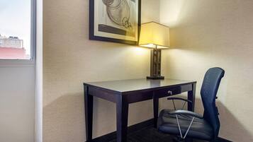 Habitación de hotel con escritorio, silla, lámpara y una obra de arte enmarcada en la pared.