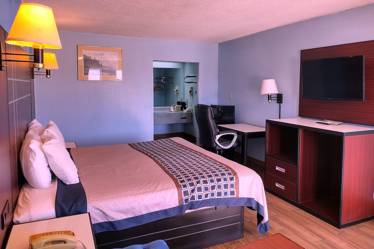 Habitación de hotel con cama, escritorio, televisor y baño visible a través de una puerta abierta.