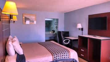A hotel room with a bed, desk, TV, and a bathroom visible through an open door.