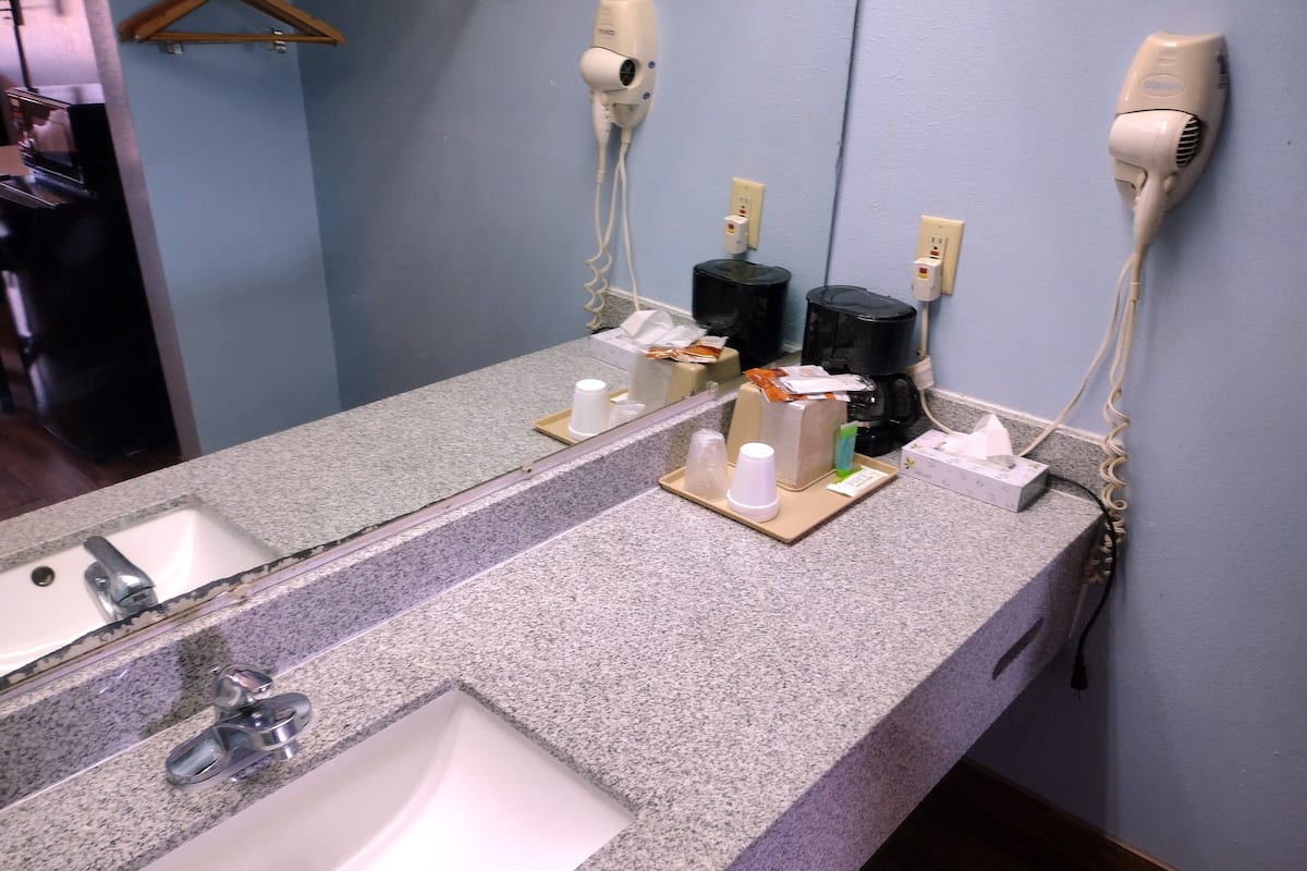 Un baño con encimera de granito, lavamanos, dos secadores de pelo y un espejo.