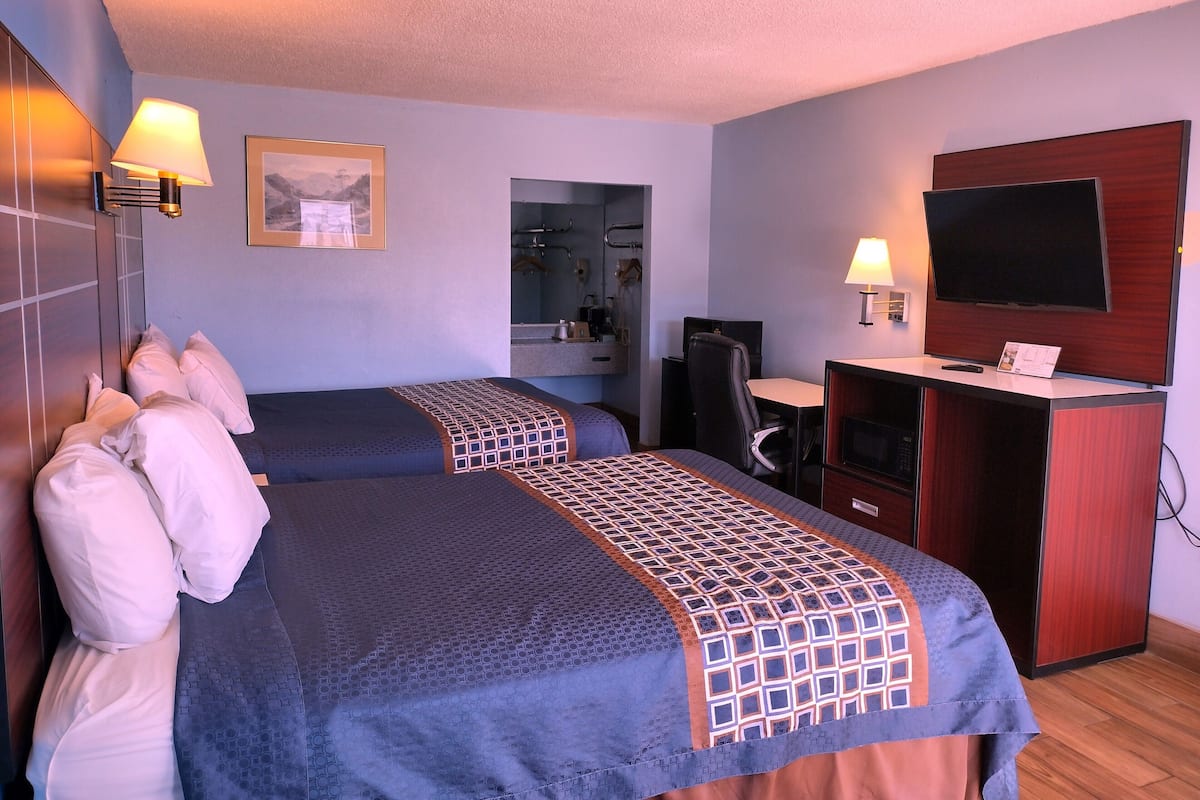 Habitación de hotel con dos camas, un escritorio, un televisor y un espejo.