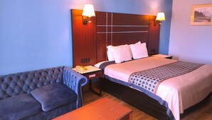 A hotel room with a bed, a sofa, a table, and two wall-mounted lamps. - Rodeway Inn Richland - Jackson South (Richland)