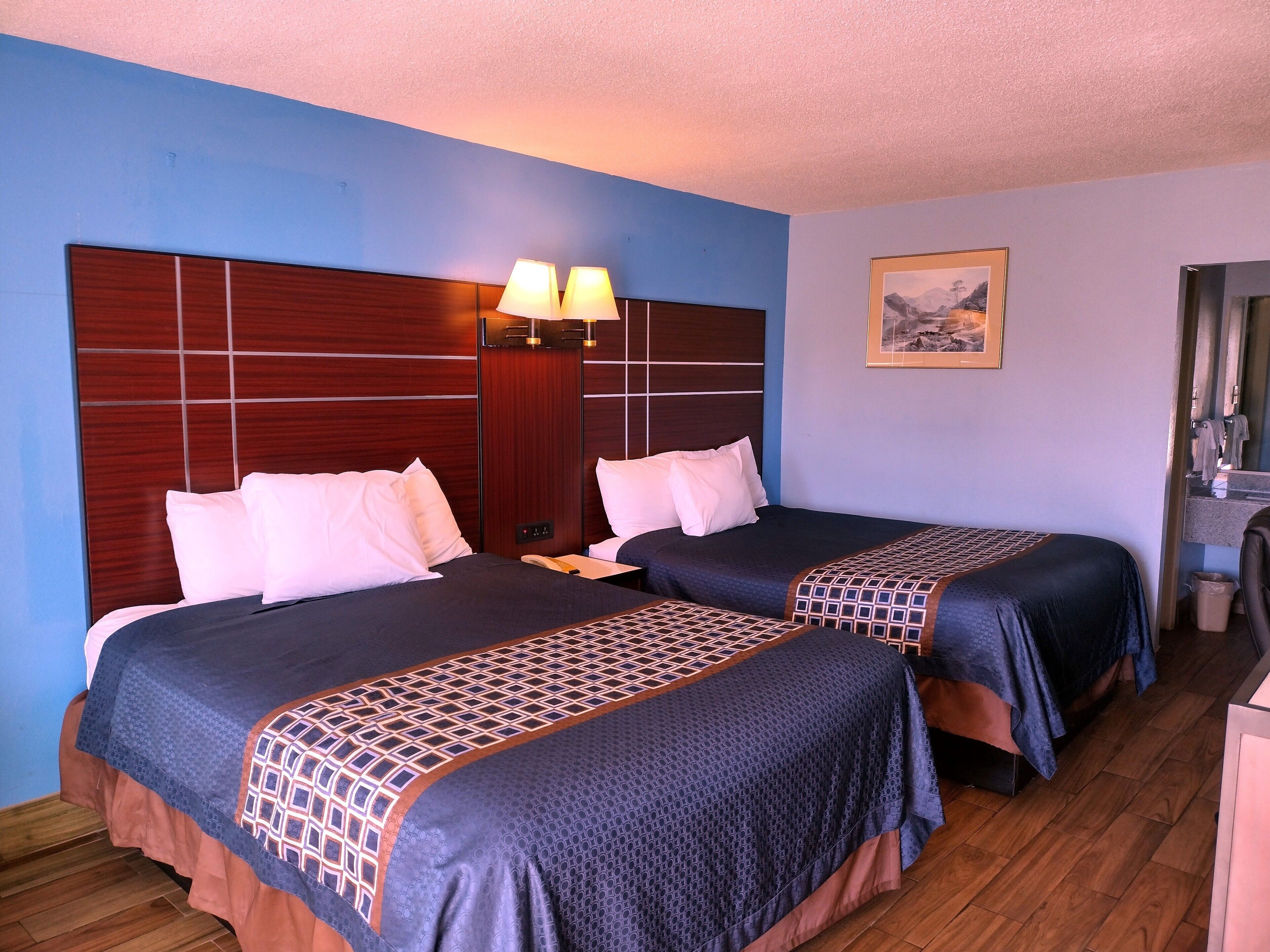 A hotel room with two beds, wooden headboards, a painting on the wall, and a desk with a chair.