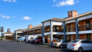 A motel with a parking lot, multiple-story buildings, and a clear blue sky.