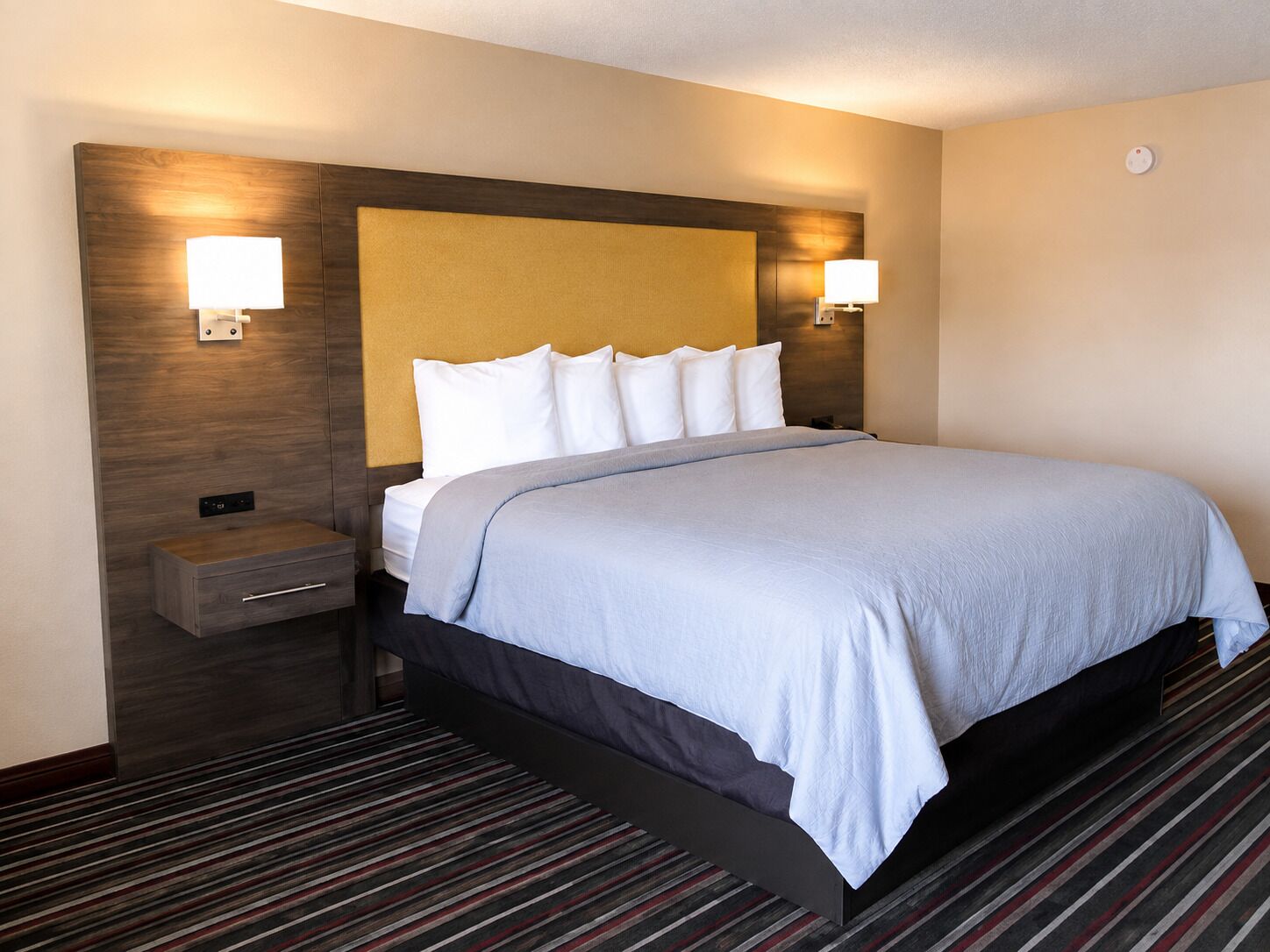 Una habitación de hotel con cama, mesitas de noche y lámparas fijadas a la pared.
