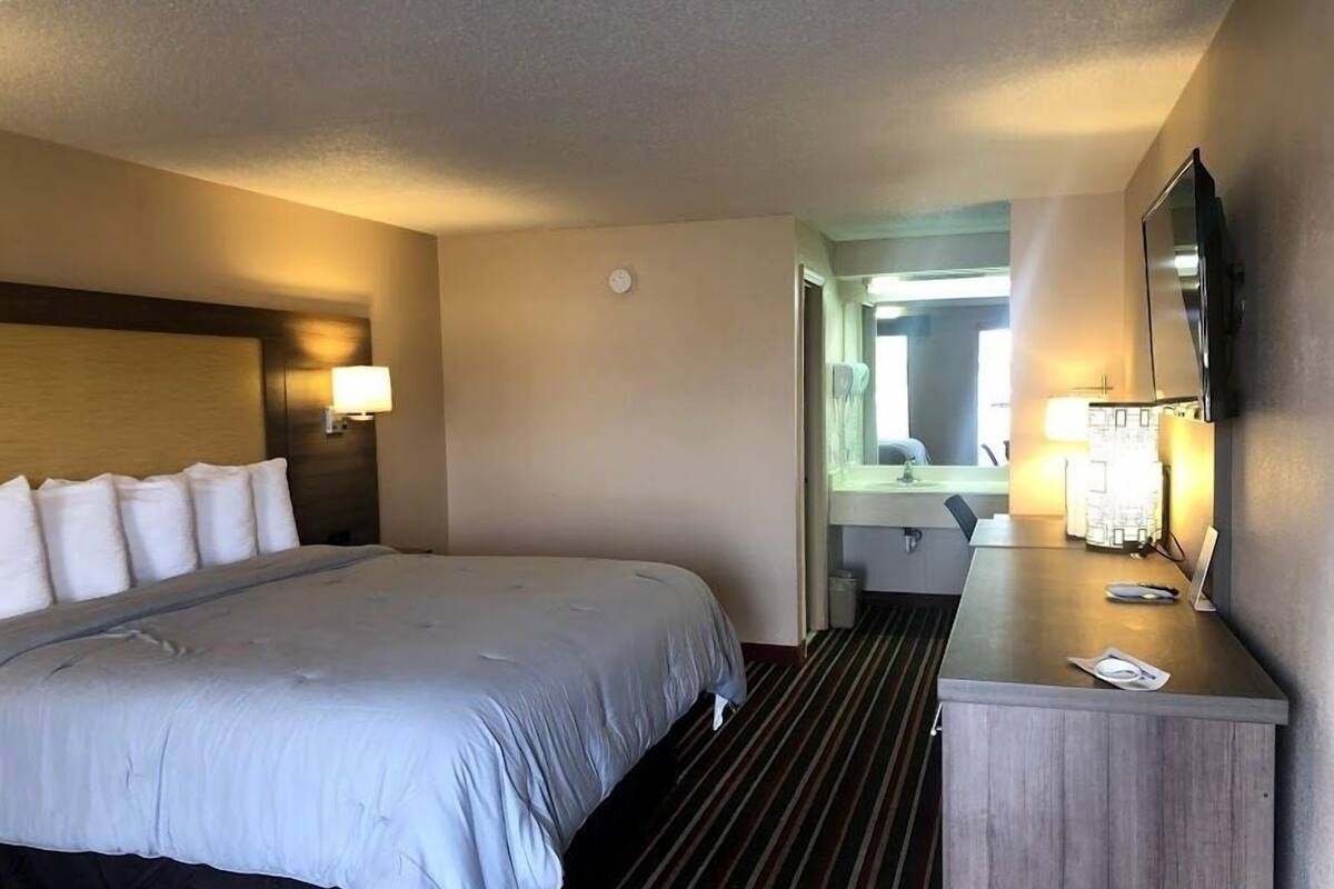 A hotel room with a bed, bedside table, lamp, and a mirror.