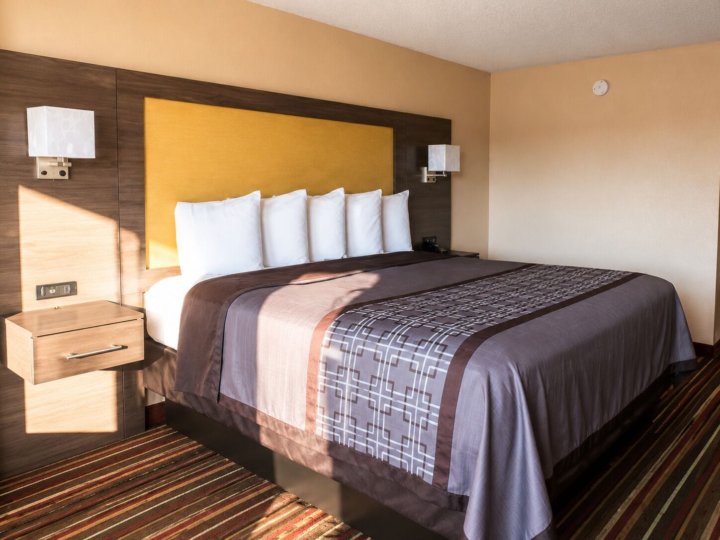 A hotel room with a bed, bedside tables, a nightstand, and a headboard.