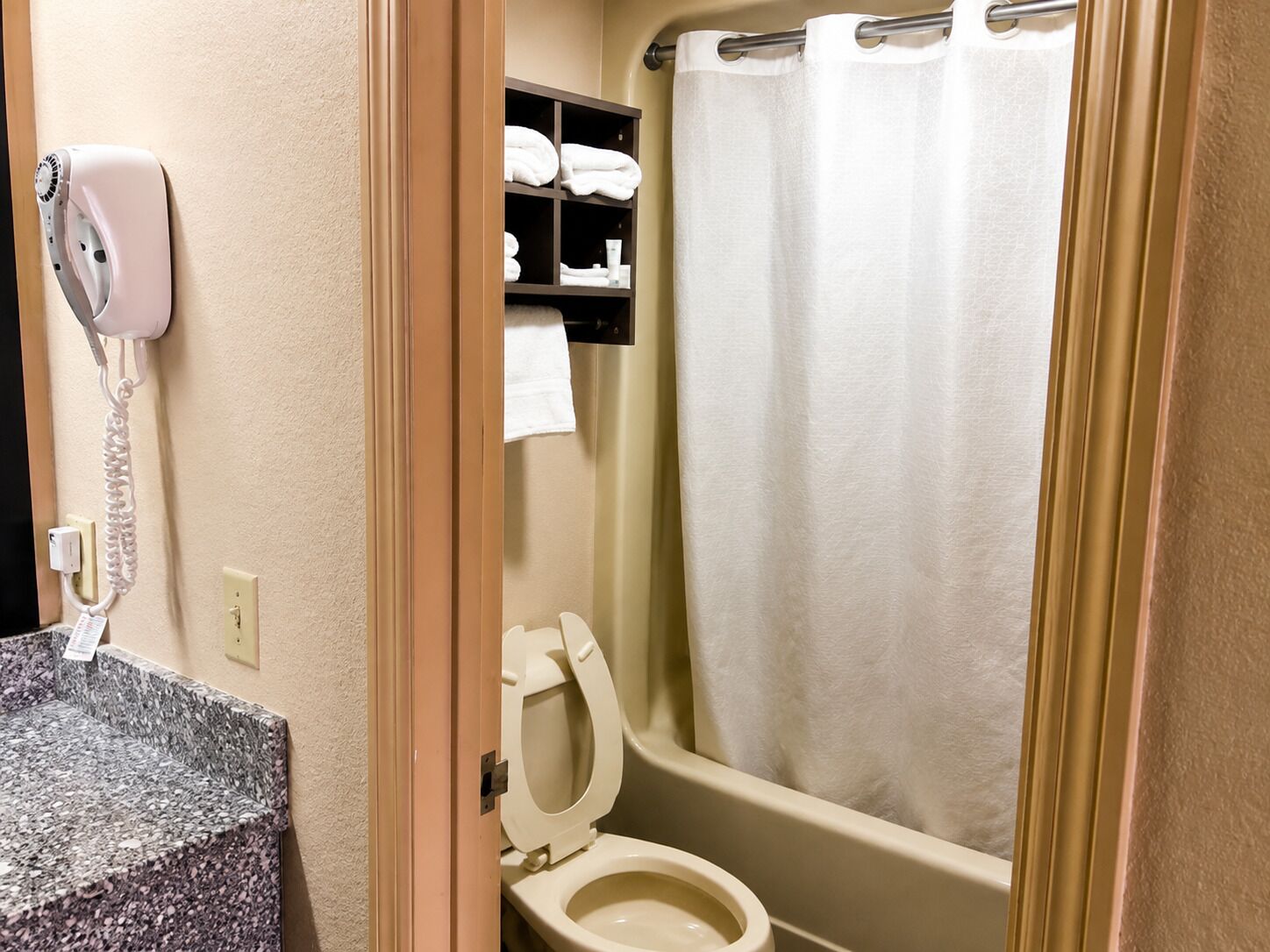 A bathroom with a toilet, a towel rack with towels, a shower curtain, and a hair dryer on the wall.
