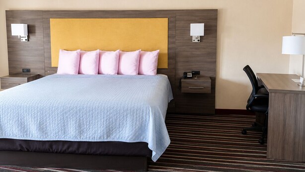 A hotel room with a bed, bedside tables, a desk, and a chair. - Legacy Inn Sumner (Gallatin)