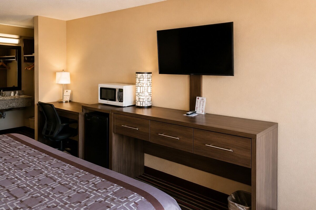 A hotel room with a bed, a desk with a microwave, a lamp, and a flat-screen TV.